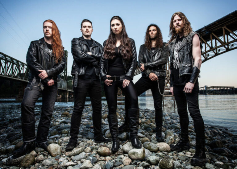 Les 5 membres du band unleash the archers qui sont positioné devant un étendu d'eau